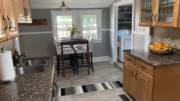A kitchen with granite countertops, a dining table with chairs, a sink, and a window with a view of greenery.