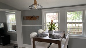 A dining area with a wooden table, white chairs, a potted plant, and a wall clock.