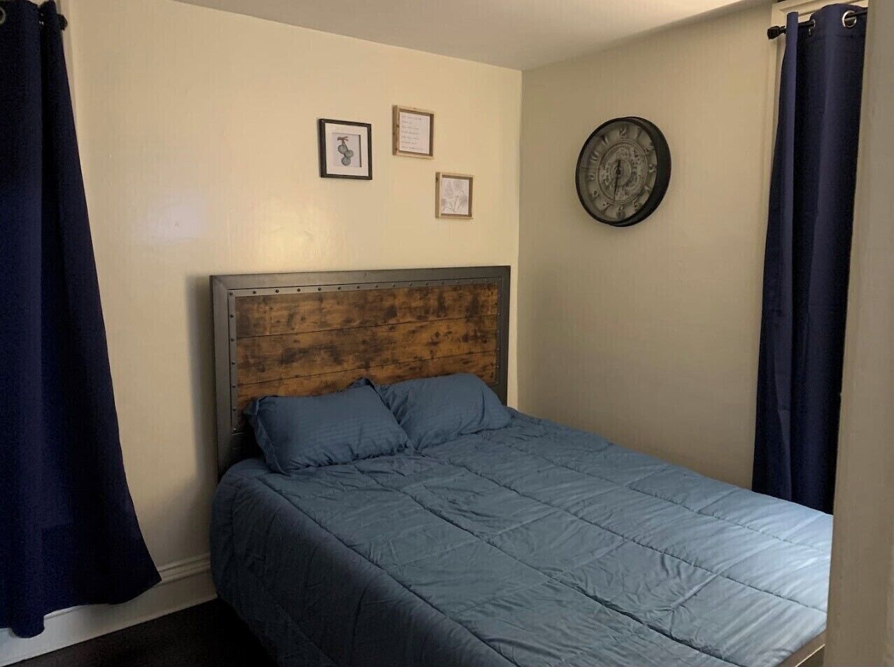A single bed with a wooden headboard, a blue bedspread, and two framed pictures on the wall.