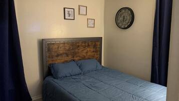 A single bed with a wooden headboard, a blue bedspread, and two framed pictures on the wall.