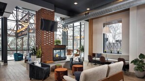 Een moderne lounge met een metselwerk open haard, zachte zitplaatsen en grote ramen met uitzicht op een industriële constructie.