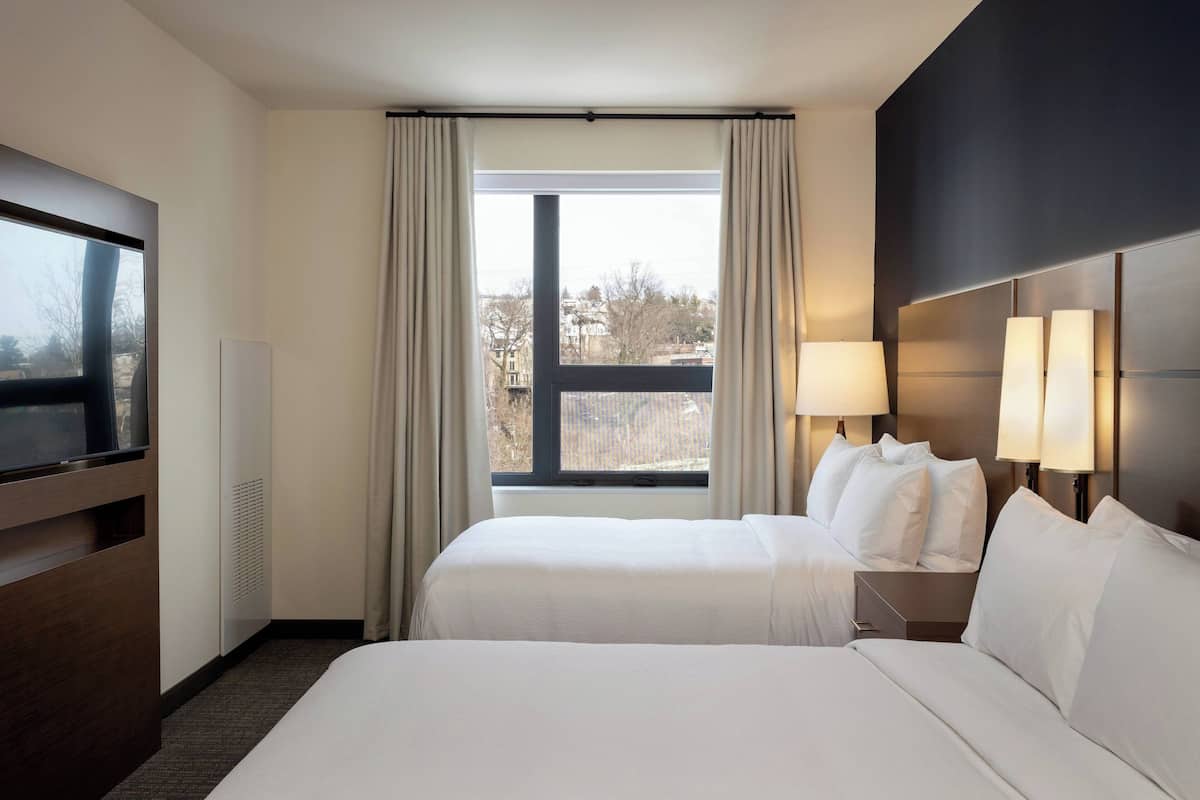 A hotel room with two beds, a TV, and a window with curtains.