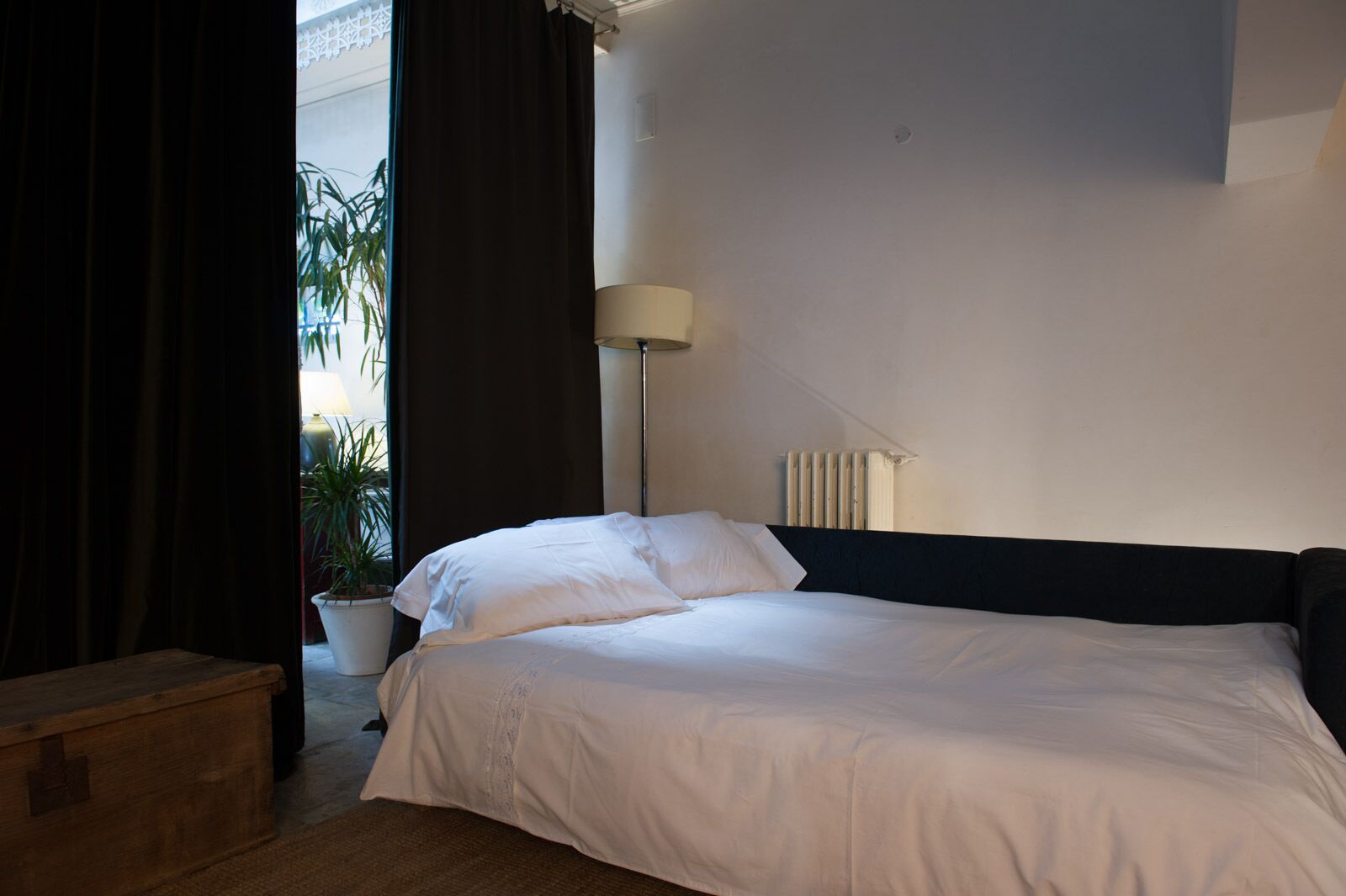 A hotel room with a bed, a lamp, a radiator, and a potted plant.