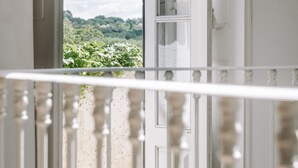 Un balcone con ringhiera bianca, pavimento in legno e vista su vegetazione e colline sullo sfondo.