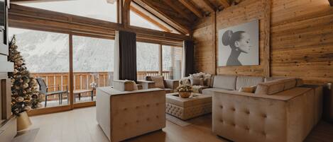 A spacious living room with a high ceiling, large windows, and a wooden interior.