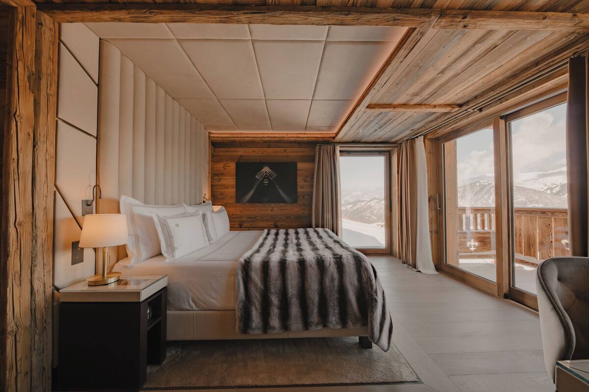 Quarto com cama grande, mesa de cabeceira, abajur e vista para o exterior.