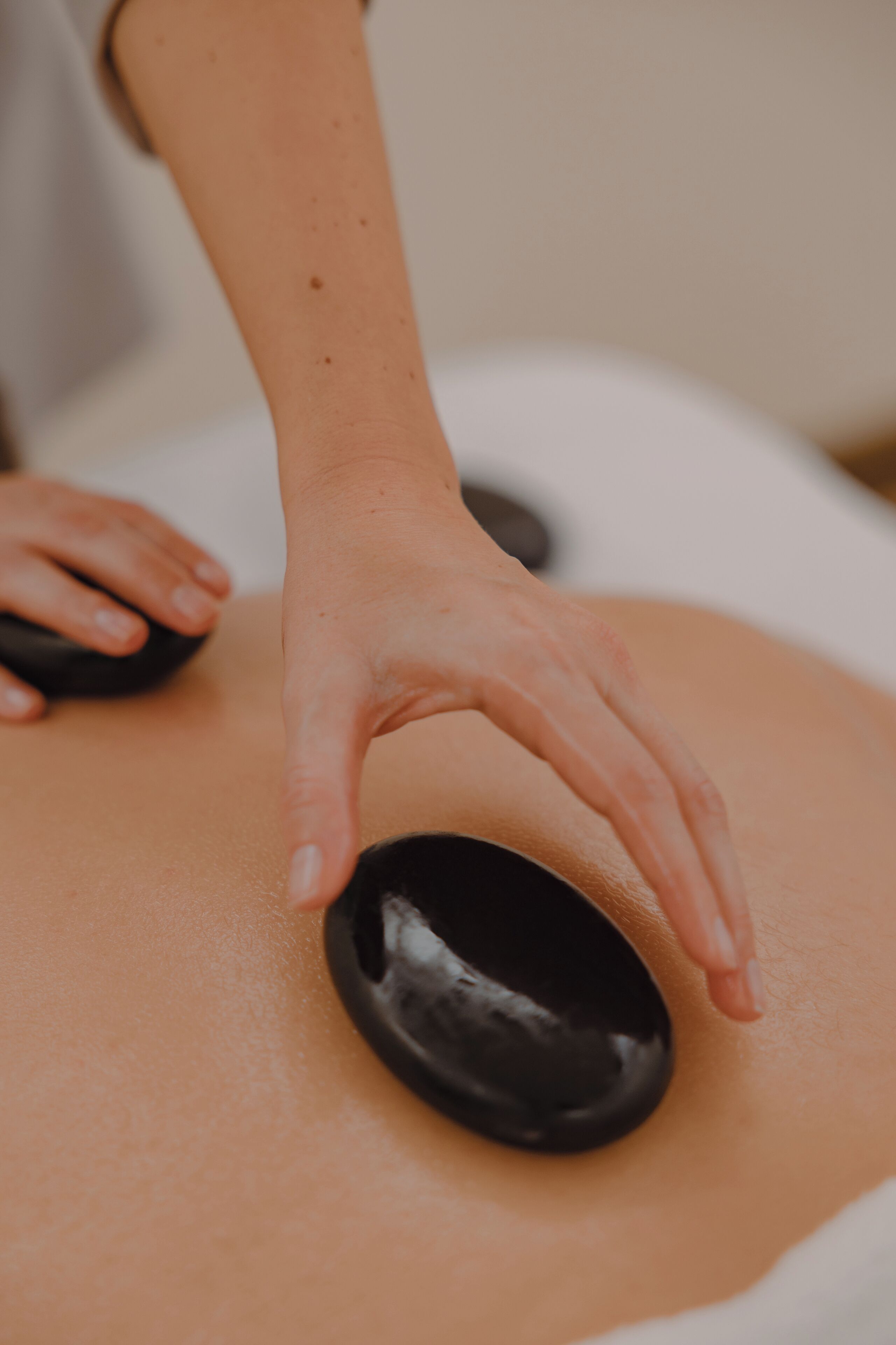 Gros plan d’une main exerçant une pression sur une pierre noire posée sur une table de massage.