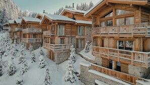 Een houten chalet met meerdere balkons en een stenen fundering, omringd door met sneeuw bedekte bomen.