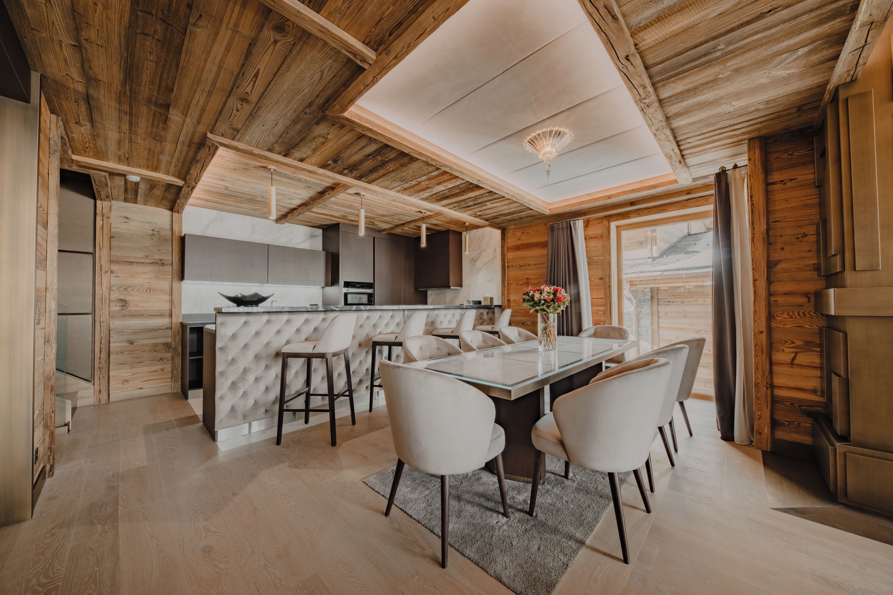 Une cuisine moderne dotée d’un îlot central, d’un plafond en bois et d’un coin repas avec une table et des chaises en verre.