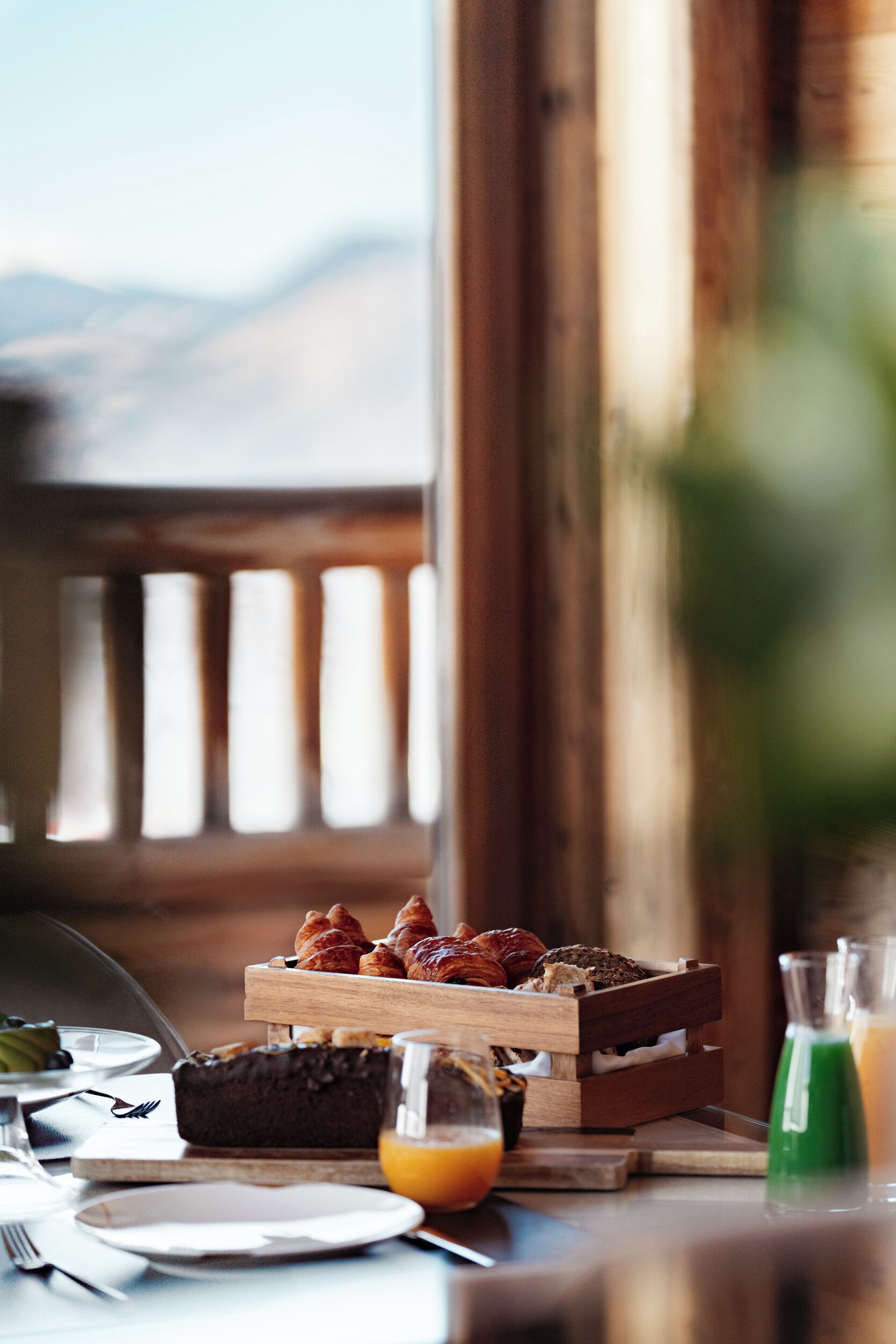 A breakfast setting with croissants, a chocolate cake, and juice glasses on a wooden table.