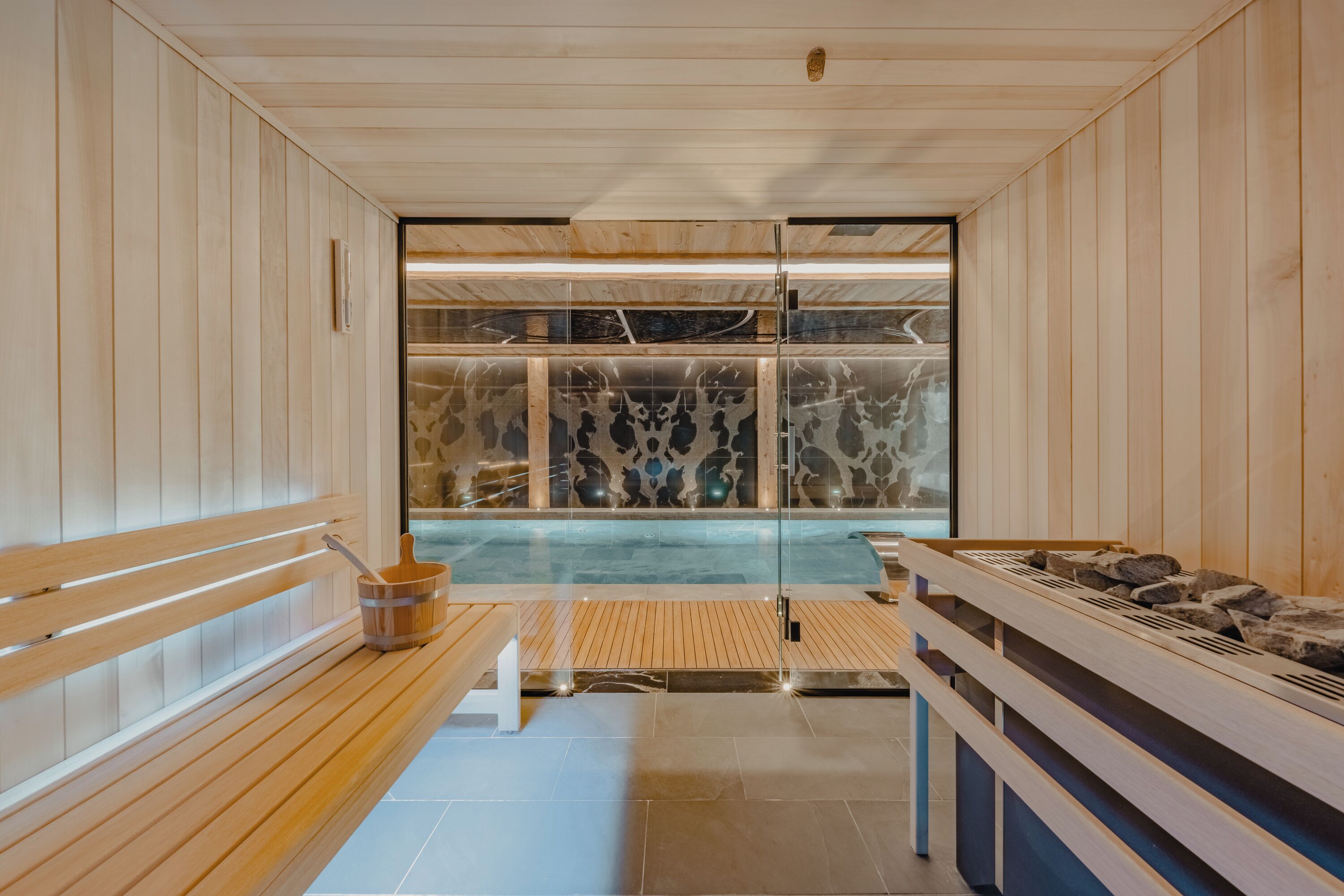 A sauna with wooden benches, a glass wall, and a stone wall in the background.