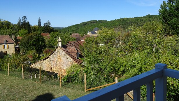 Ein aus Stein gebautes Haus mit Ziegeldach, umgeben von Grün und weiteren Häusern in einer hügeligen Landschaft.