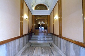 A marble-floored hallway with a wooden door at the end, flanked by wall sconces.