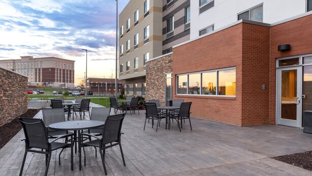 Un patio al aire libre con mesas y sillas, un edificio de ladrillo y un estacionamiento al fondo.