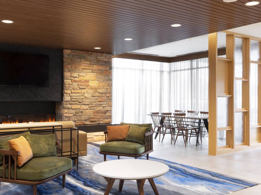 A modern lounge area with a stone wall, a fireplace, comfortable seating, and a large window providing natural light.