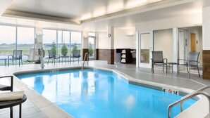 Una piscina interior con agua azul cristalina, rodeada de sillones de descanso y vistas al exterior.