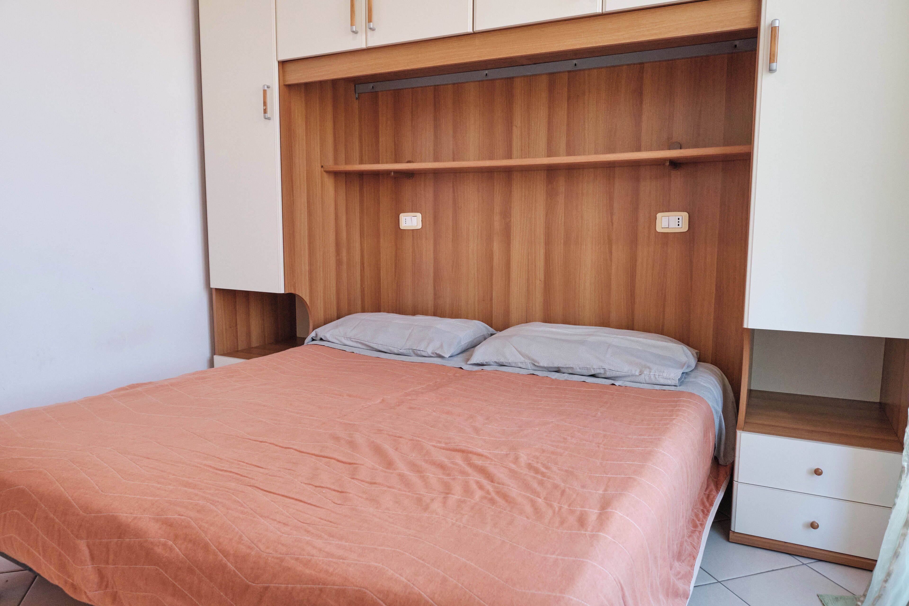 A bedroom with a bed, a wooden headboard, a nightstand, and a drawer unit.
