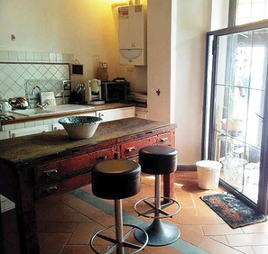 A kitchen with a tiled backsplash, a large island with stools, a refrigerator, and a window with a view of the outdoors.