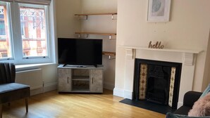 A living room with a fireplace, a television on a stand, and a sofa. - Central Location - 2 Bedroom Apartment (Reading)