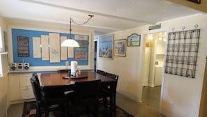 Un coin repas avec une table et des chaises en bois, un tapis à motifs et des éléments décoratifs sur les murs, notamment des tableaux encadrés et un mur bleu orné de texte.
