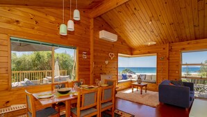A wooden cabin with a dining area, a sofa, and a view of the ocean.