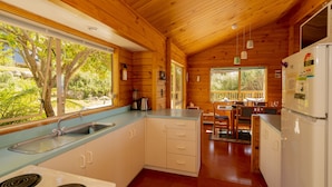 A wooden cabin kitchen with a sink, stove, refrigerator, and dining area.