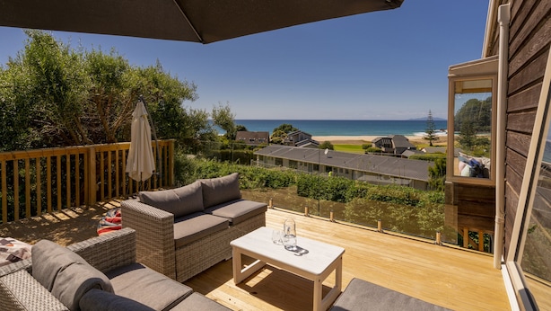 A balcony with wicker furniture, a table, and a view of the beach and ocean.