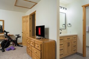 Une pièce comprenant une commode en bois, un téléviseur, un vélo et une salle de bain avec un miroir et des placards.