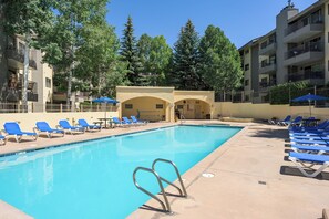 A swimming pool with blue lounge chairs, a covered seating area, and a building with balconies. - BC/Avon Mtn Gem-3BR/Pool/Hot Tub/Ski Shuttle/Sauna/Gondola Walk! (Avon)