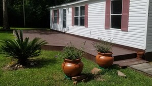 A white mobile home with red shutters, a paved driveway, and two large terracotta pots with plants. - Clean and Cozy Creekside Home (Conroe)