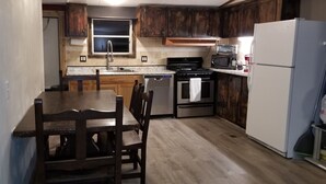 A compact kitchen with wooden cabinets, a stainless steel refrigerator, a microwave, a stove, and a dishwasher. - Clean and Cozy Creekside Home (Conroe)