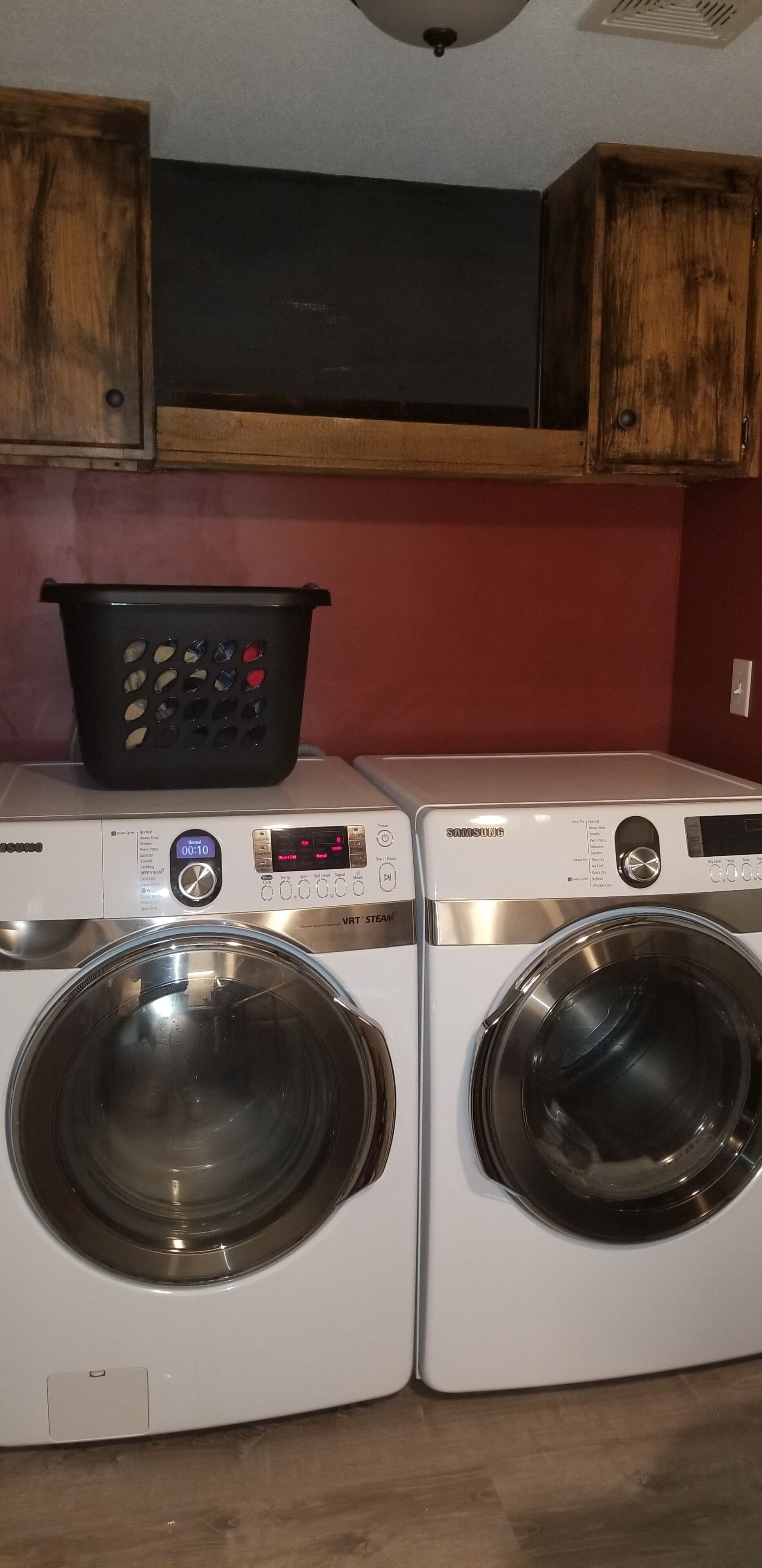 Deux machines à laver à chargement frontal dotées d’écrans numériques, un panier à linge noir et des armoires en bois au-dessus.