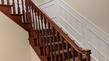 Un escalier en bois, avec un palier recouvert de moquette et un mur blanc orné d’une petite fenêtre.