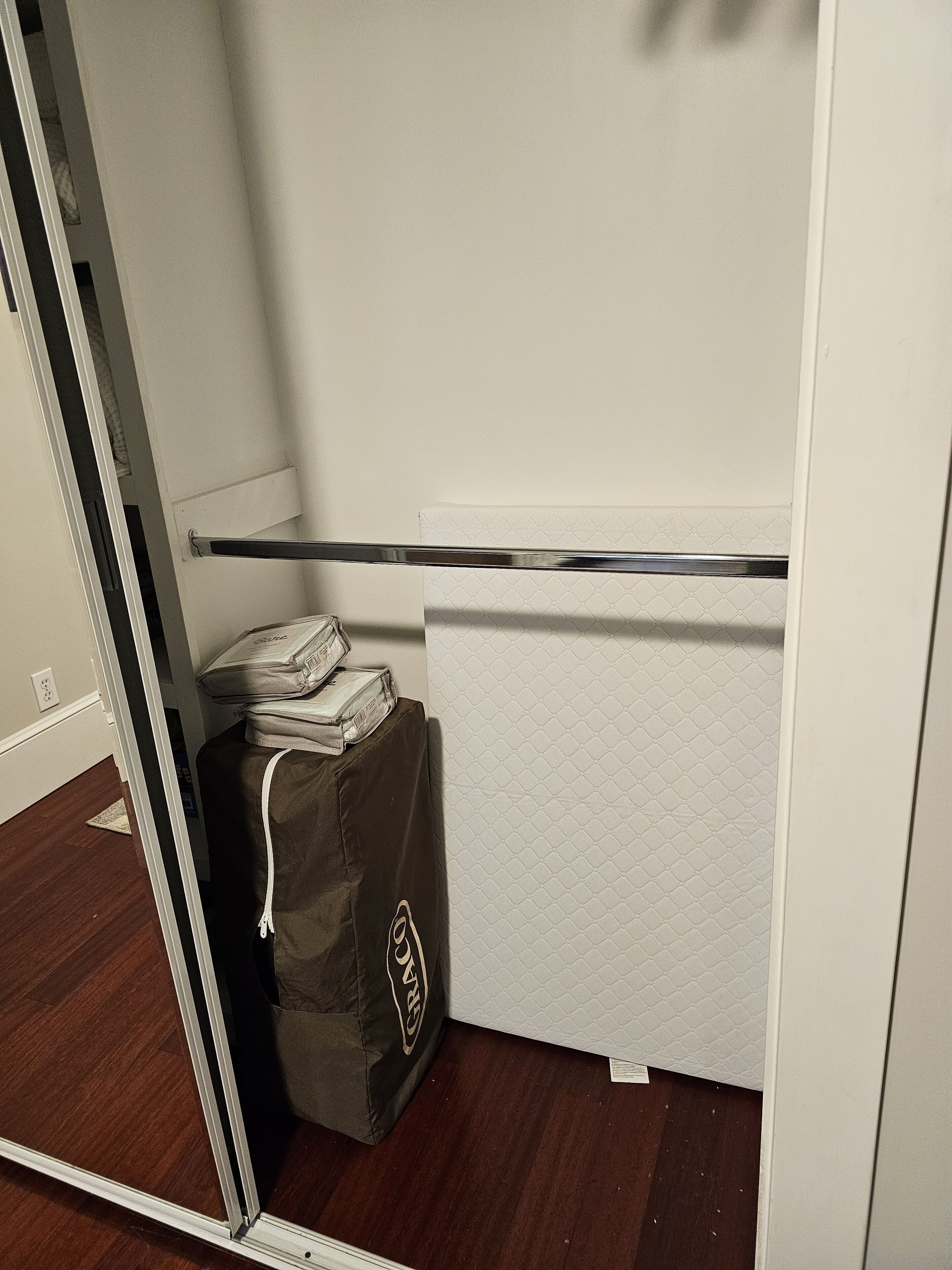 A closet with a hanging rod, a stack of folded clothes, and a storage bag.