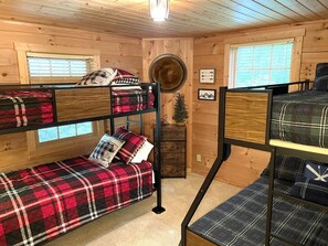 Une cabine équipée de deux lits superposés, d’une petite commode et d’une fenêtre avec des stores.