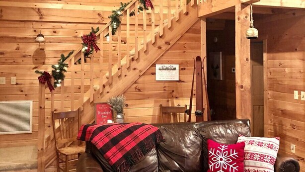Un interior de cabaña acogedor con una escalera de madera, sofá de cuero y decoración festiva.