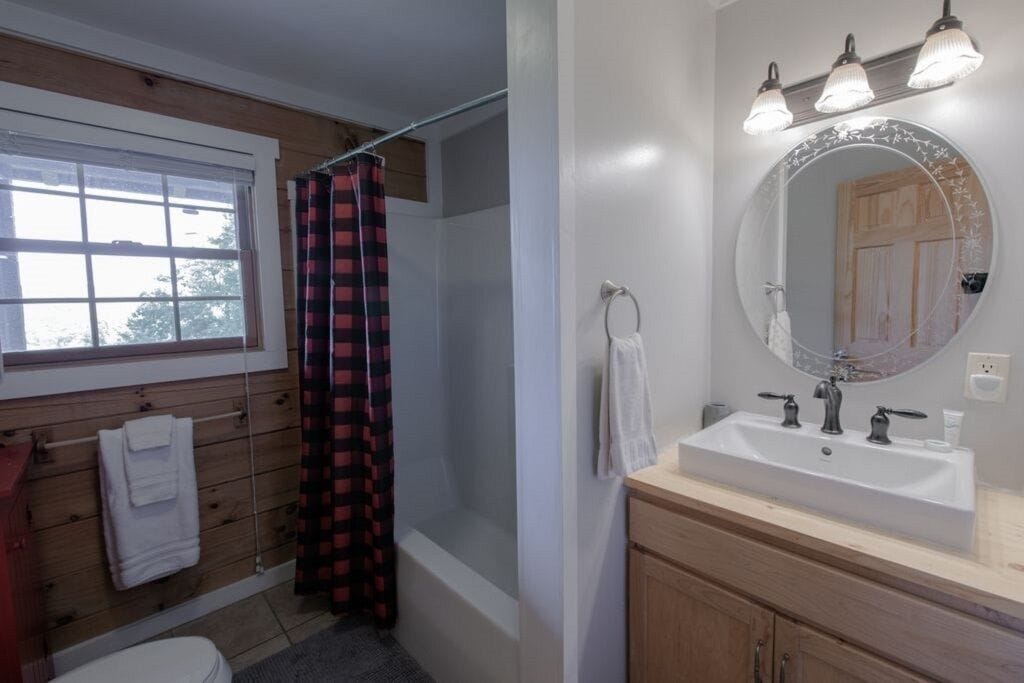 A bathroom with a wooden vanity, a white sink with a round mirror, and a shower curtain.