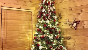 Un interior de cabaña acogedor con un árbol de Navidad decorado, un sillón escocés con un cartel que dice 'Feliz Navidad' y un sofá de cuero.