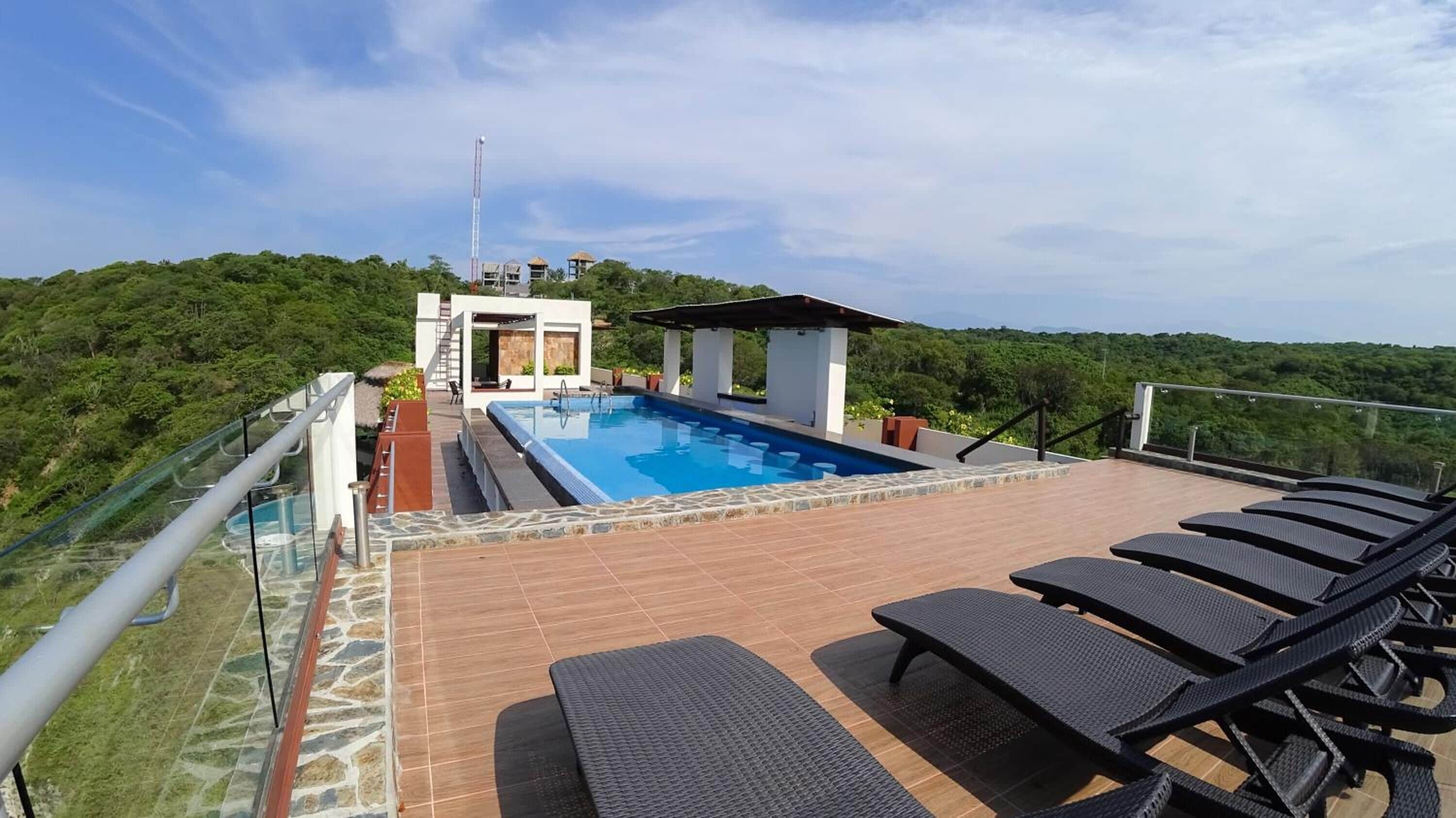 Una piscina sul tetto con lettini, un parapetto in vetro e vista su un lussureggiante spazio verde.