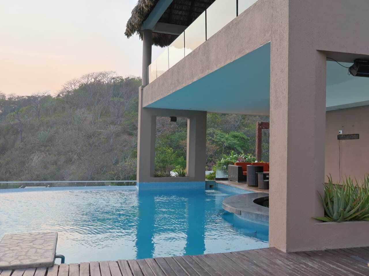 Un área de piscina exterior moderna con terraza de madera, rodeada por una estructura de hormigón y vistas a una ladera.