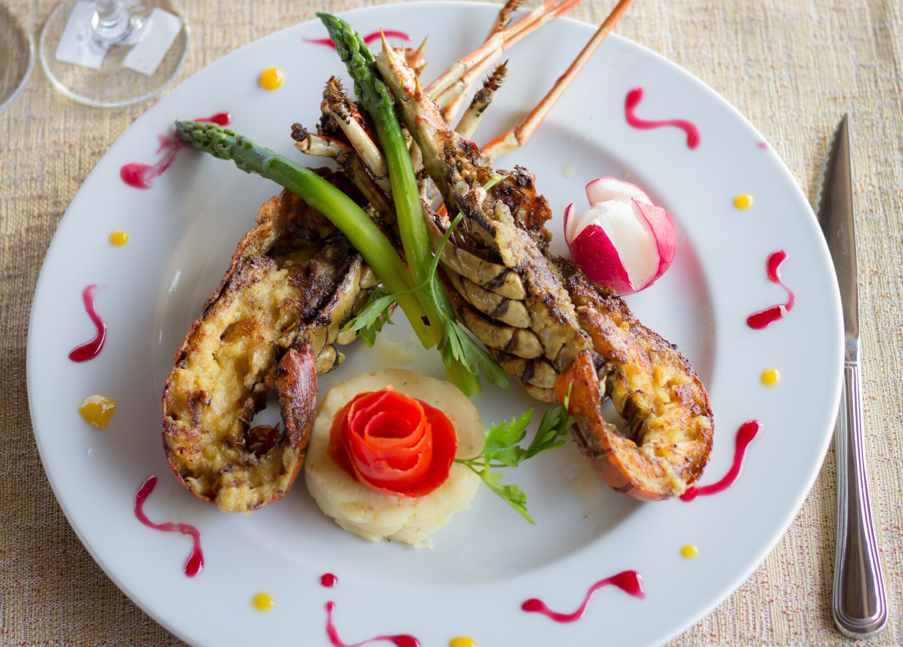 Une assiette de homard, accompagnée d’asperges et de radis, présentée sur une assiette blanche avec une sauce rouge et jaune.