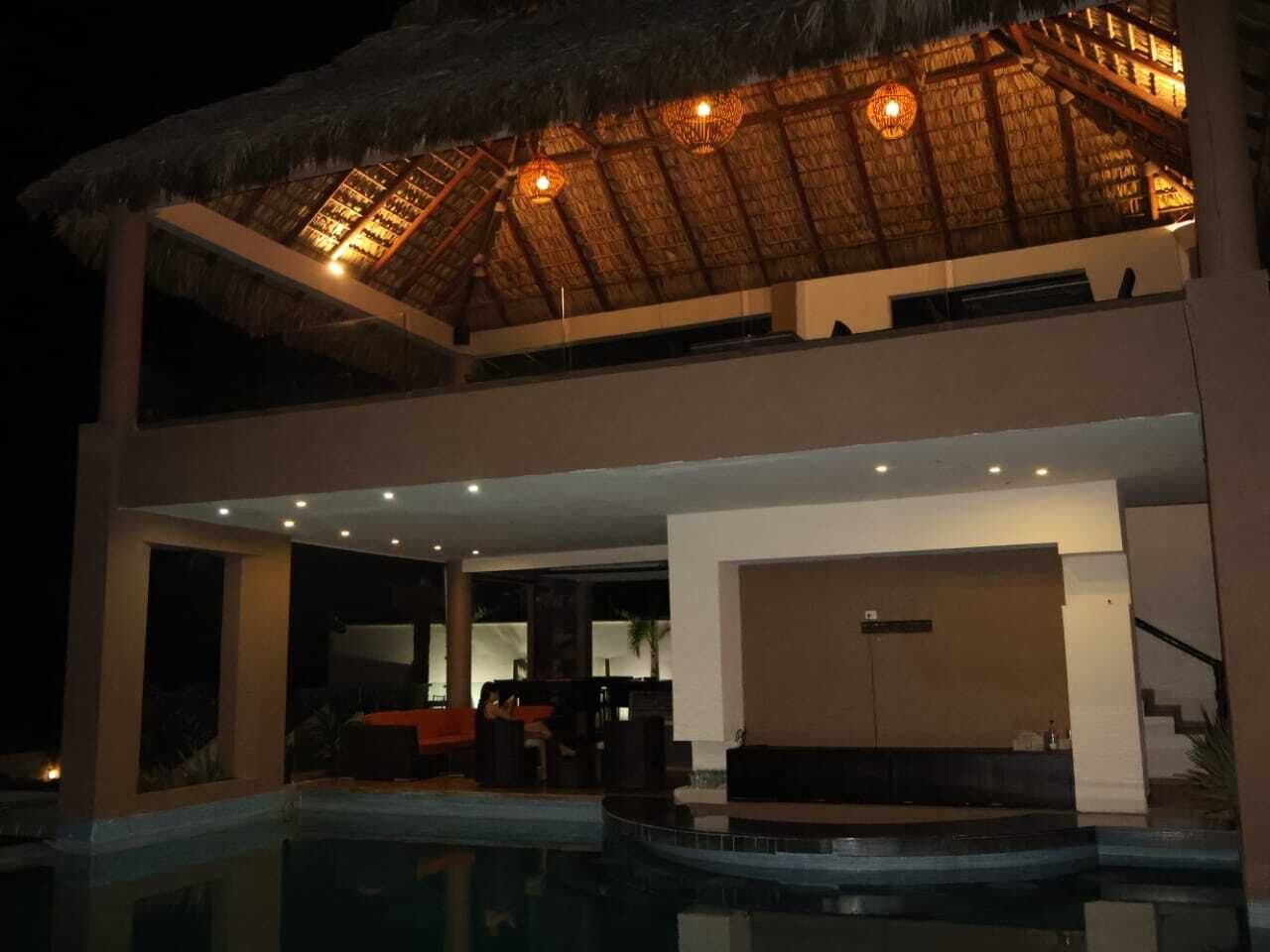 Un edificio de dos pisos con piscina, techo de paja y zona de bar.