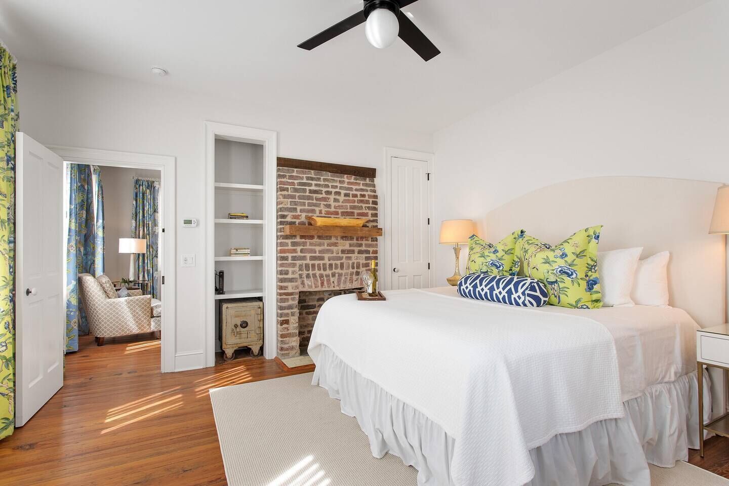 A bedroom with a white bed, a brick fireplace, and a wooden floor.