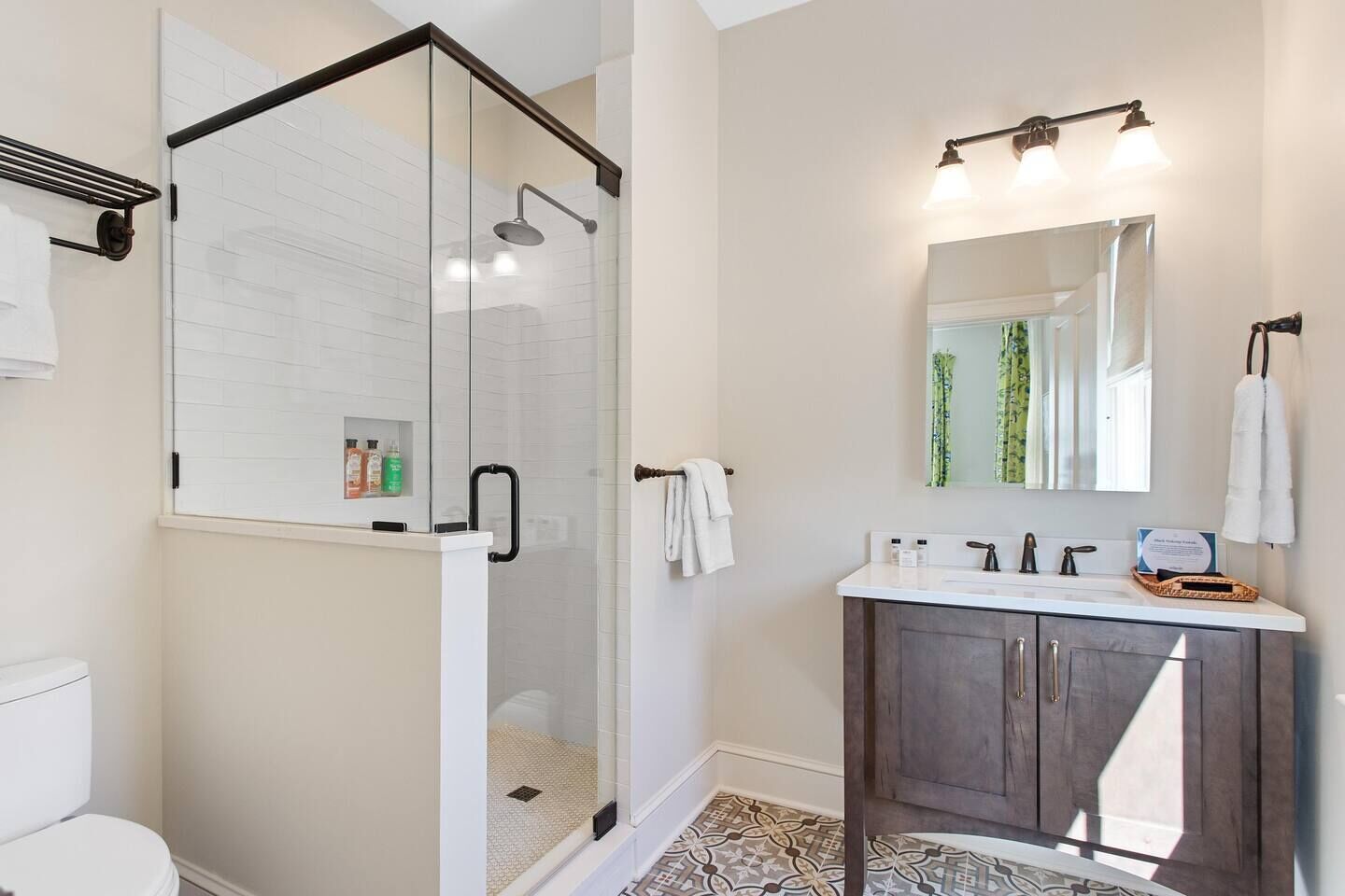 A modern bathroom with a glass-enclosed shower, a vanity with a mirror, and a tiled floor.