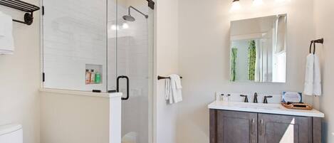 A modern bathroom with a glass-enclosed shower, a vanity with a mirror, and a tiled floor.