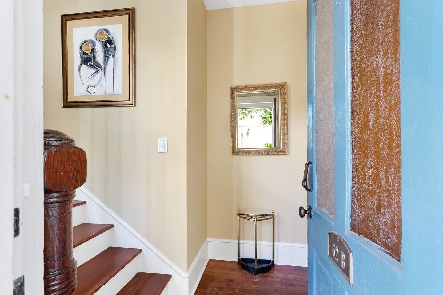 A staircase with wooden steps and a wooden handrail, leading to a door with a blue frame and a brass plate.