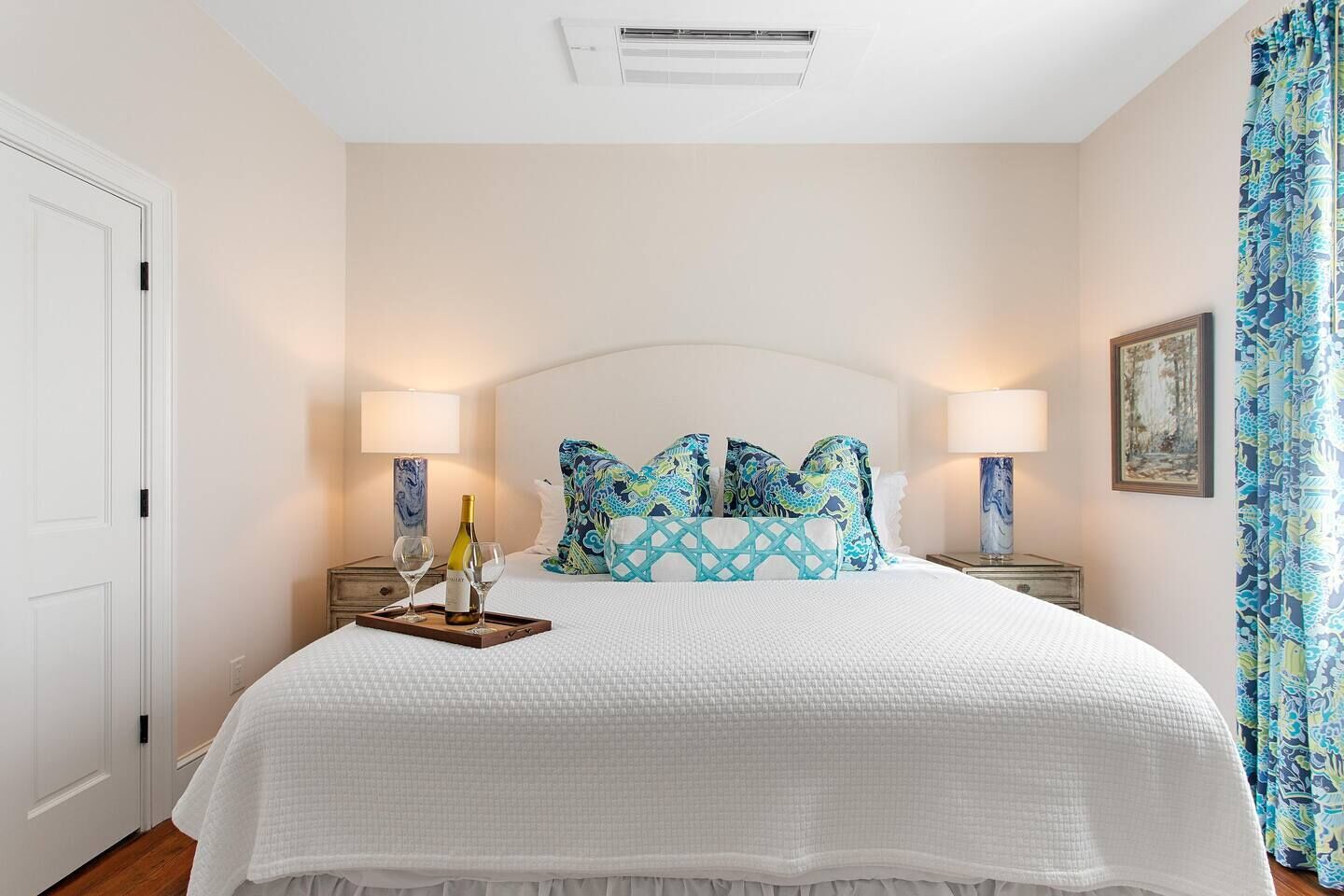 A hotel room with a large bed, two bedside tables, a nightstand, a wall-mounted air conditioner, and a window with curtains.