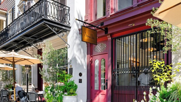 Un café con terraza, puerta roja y plantas en macetas.
