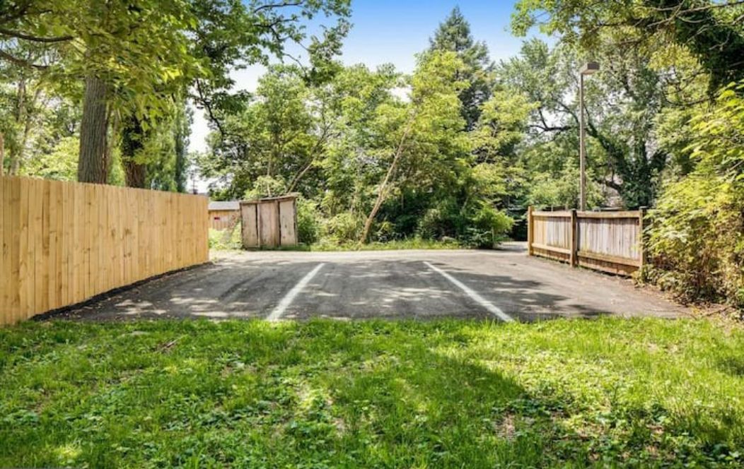 A fenced backyard with a paved area, surrounded by trees and greenery.