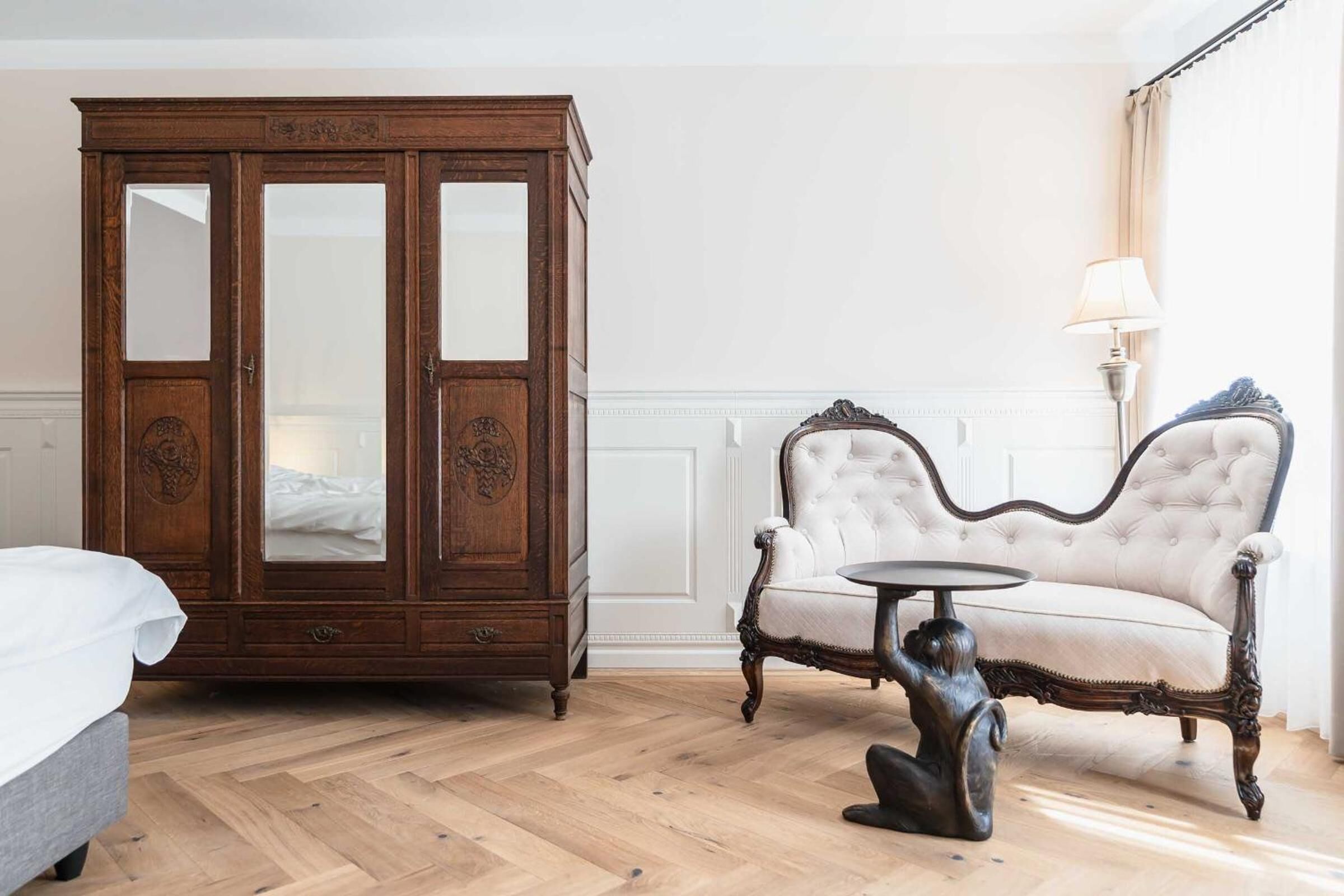 Een kamer met een grote houten garderobe, een witte gestoffeerde bank en een kleine ronde tafel.